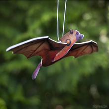Load image into Gallery viewer, Bat-shaped paper air freshener with 3D wings. Item is hanging from a white string against a blurred, green leaf backdrop.