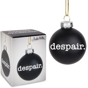 A black christmas ornament with white serif font type reading "Despair." The glass ball has a decorative silver loop and gold string. The black and white box with a picture of the ornament is also included.