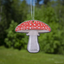 Load image into Gallery viewer, A paper air freshener shaped like a fly agaric or amanita mushroom, also called a Toadstool. It is white and red set against a blurred green leaf backdrop.